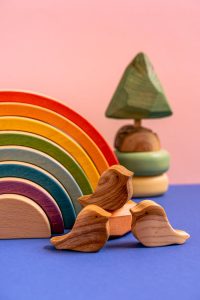 Vibrant still life of wooden toys with birds, rainbow, tree, on a blue surface.