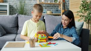 Cheerful girl mother is playing with little son with wooden blocks and laughing enjoying educational activity. Happy family, people and interesting toys concept.